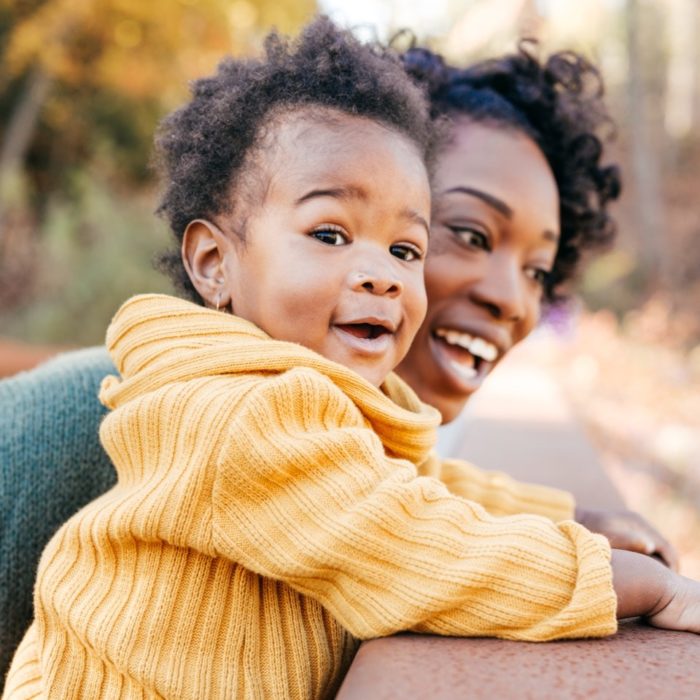 A woman smiles with her young child outside.