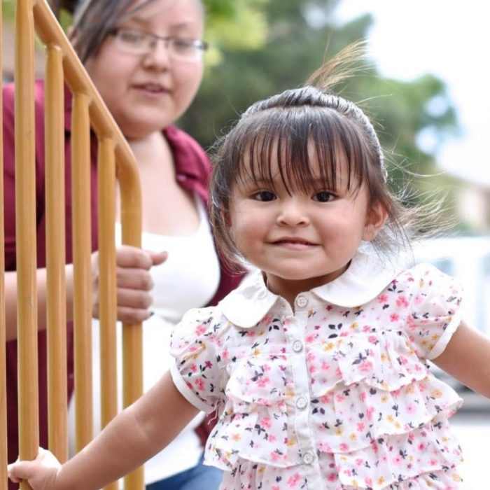 A young girl looks at the camera while her mother watches.